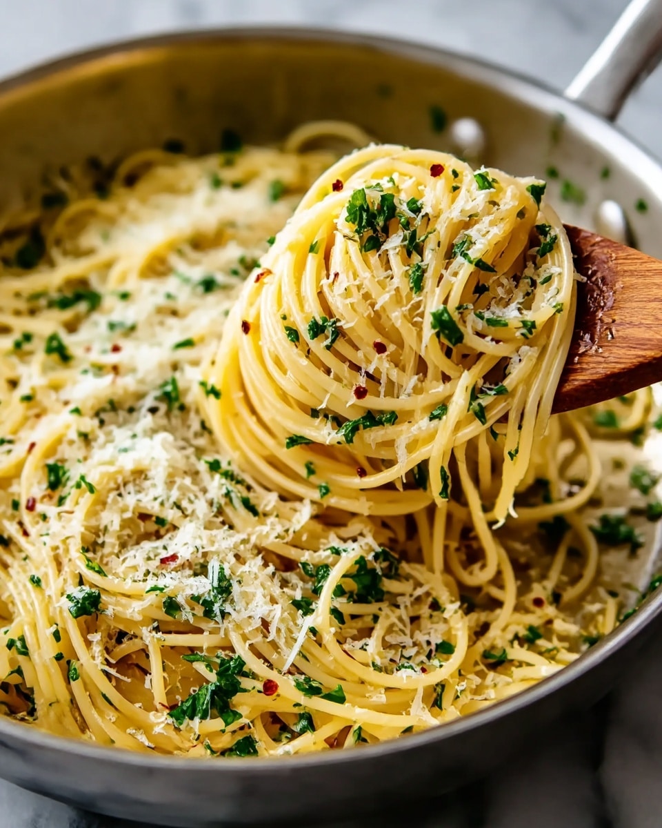 A close-up of a pan filled with spaghetti pasta tossed in a light sauce, with the noodles coated in shiny oil and some small red pepper flakes scattered throughout. Fresh green parsley pieces are sprinkled generously on top, adding bright color. There is a layer of finely grated white cheese lightly covering the noodles. A wooden spoon is lifting a twisted bunch of pasta in the center right, showing the smooth texture of the noodles and the loose sauce clinging to them. The pan rests on a white marbled surface. Photo taken with an iphone --ar 4:5 --v 7