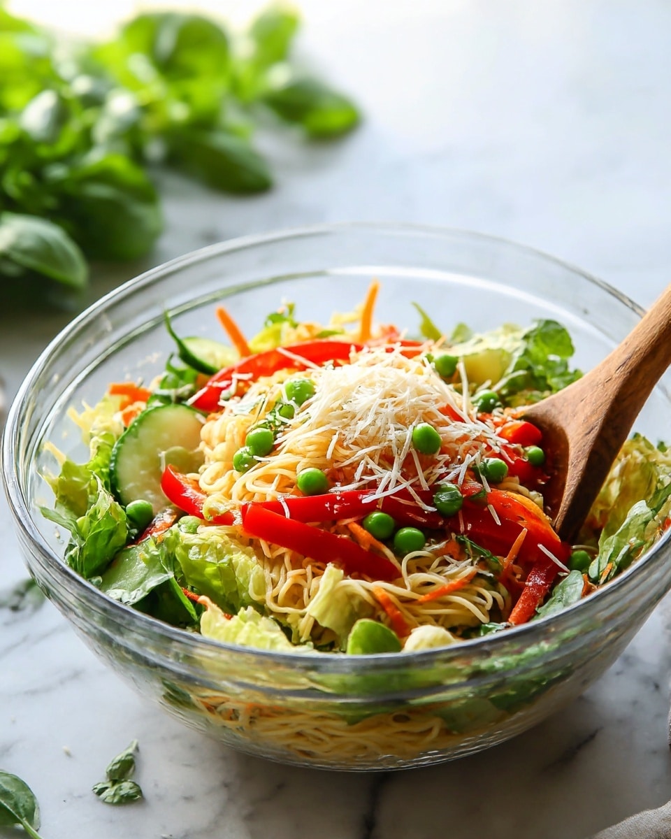 A clear glass bowl filled with a colorful mixed salad sits on a white marbled surface, with a wooden spoon inside the bowl. The salad has many layers: at the bottom are thin, pale yellow noodles, topped with bright green leafy lettuce. On top of this are red bell pepper strips and small green peas scattered around. There are slices of cucumber mixed with the vegetables, and the salad is sprinkled with light, shredded white cheese. Fresh green herbs and thin carrot strips add more color and texture throughout the bowl. In the background, green leaves are slightly blurred with natural light shining on the bowl. photo taken with an iphone --ar 4:5 --v 7