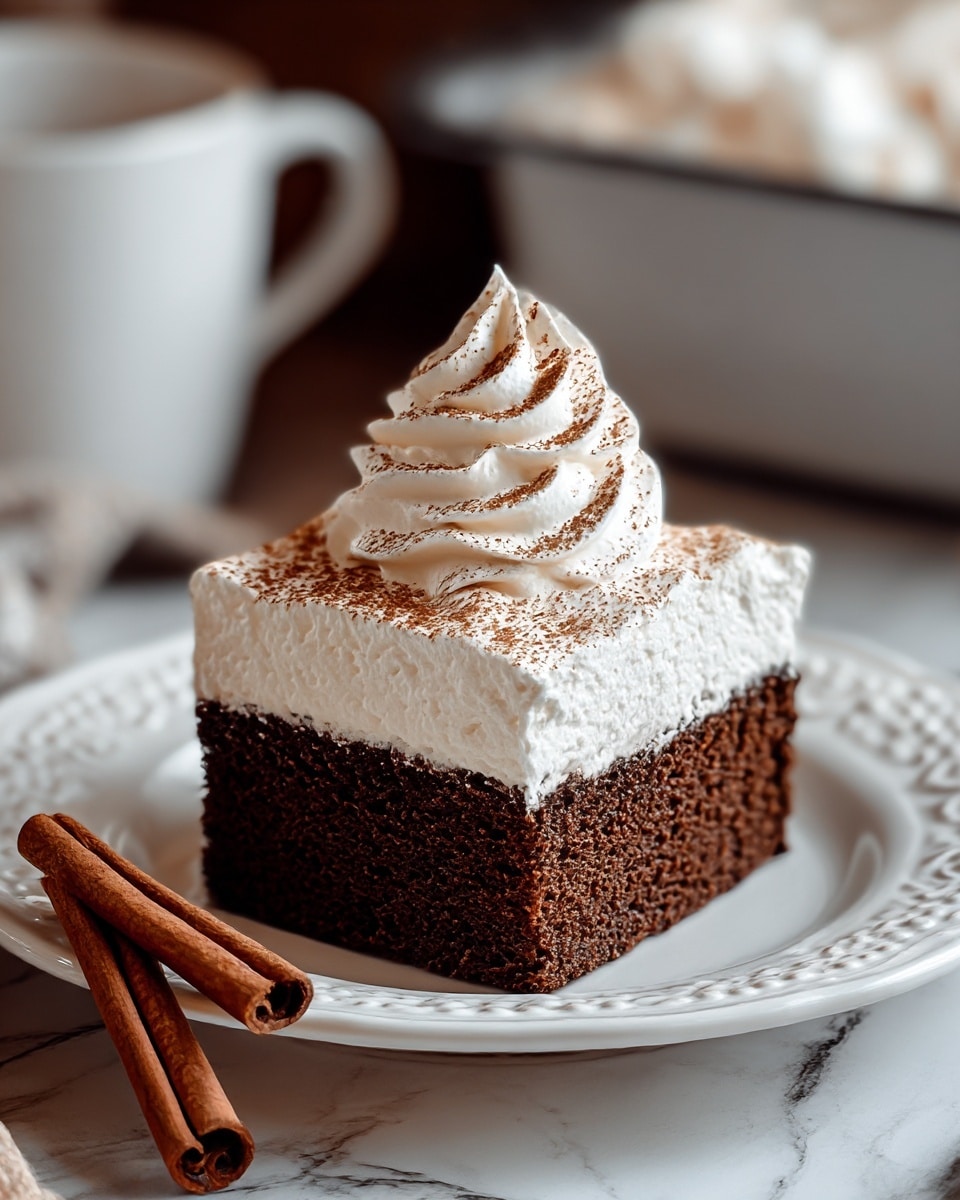 A square, two-layer cake slice is placed in the center of a white plate with a decorative edge. The bottom layer is a dark brown, spongy chocolate cake that looks moist and dense. The top layer is thick white whipped cream that is smooth and spread evenly. On top, there is a tall swirl of more white whipped cream sprinkled with fine brown cocoa powder. Around the plate, two cinnamon sticks are placed on a white marbled surface. The background includes a blurred white cup and a pan filled with whipped cream. Photo taken with an iphone --ar 4:5 --v 7