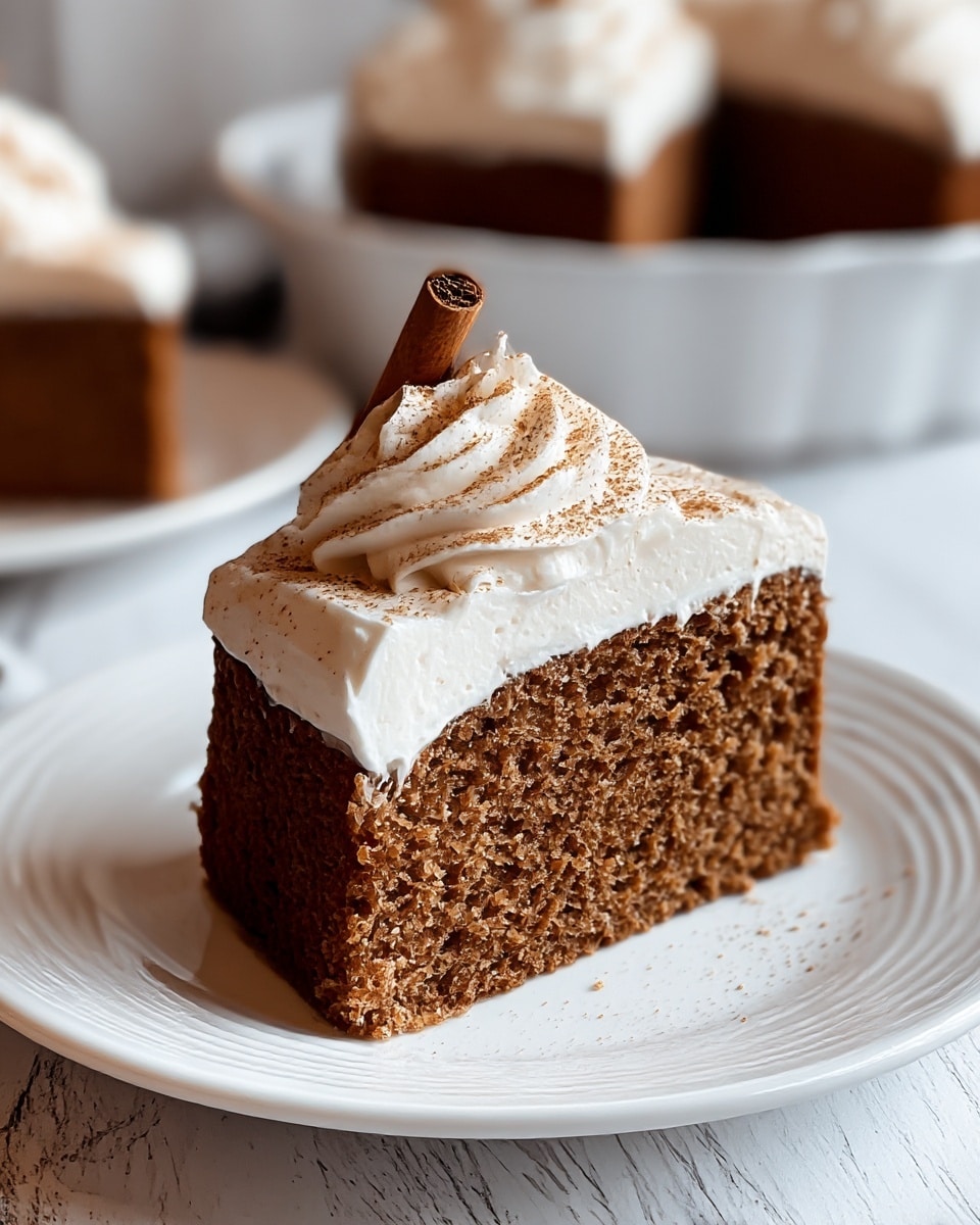 A close-up of a single slice of brown cake with a dense texture on a white plate, topped with a thick layer of smooth white frosting. On top of the frosting is a swirl of whipped cream with a light dusting of brown powder and a small cinnamon stick placed diagonally. In the background, there is a white dish with more slices of the same cake. The setting has a white marbled surface underneath the plate. photo taken with an iphone --ar 4:5 --v 7