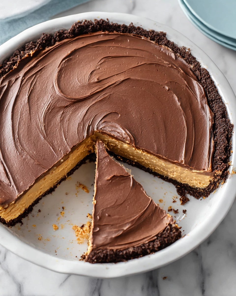 A round pie in a white dish with a dark crumbly crust forming the first layer, a thick light brown peanut butter filling as the second layer, and a smooth, swirled dark chocolate frosting spread evenly on top as the third layer. One slice is slightly lifted showing the thickness of each layer, with some crumbs scattered around the pie edge on a white marbled surface. Photo taken with an iphone --ar 4:5 --v 7
