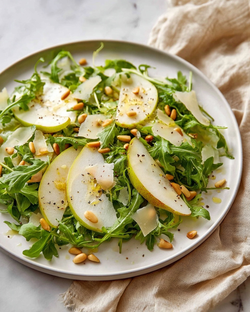 A white plate holds a fresh salad with three main layers: the bottom layer is bright green arugula leaves with a slightly crinkled texture, spread evenly across the plate; the middle layer features thinly sliced pear wedges with light greenish-yellow skin and a juicy, translucent white inside, arranged neatly on top of the arugula; the top layer includes scattered pine nuts and irregular, thin shavings of pale yellow cheese, all sprinkled lightly with black pepper and a drizzle of dressing that gives a slight shine. The plate sits on a white marbled surface with a soft beige cloth nearby. photo taken with an iphone --ar 4:5 --v 7
