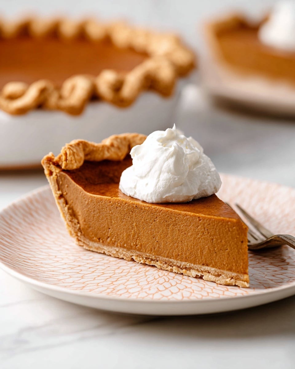 A single slice of pumpkin pie sits on a white plate with a subtle geometric pattern. The pie has three distinct layers: a thin, light brown, crumbly crust at the bottom; a thick, smooth, medium brown pumpkin filling in the middle; and a dollop of white whipped cream on top, slightly swirled and soft in texture. The edges of the pie crust are crimped and golden brown. A silver fork lies next to the pie slice on the plate. In the background, a full pumpkin pie with a similar crust can be seen in a white pie dish, all set on a white marbled surface. photo taken with an iphone --ar 4:5 --v 7