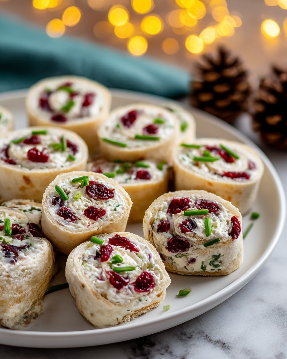 A close-up view of a white rolled appetizer held by a woman's hand, showing three visible layers: a light beige outer wrap, a thick middle layer of creamy white cheese mixed with green herbs, and scattered dark red dried cranberries embedded throughout. The roll is round and sliced evenly, revealing the spiral inside. In the background, several similar rolls are arranged on a white plate on a white marbled surface with soft warm bokeh lights and green pine branches softly blurred in the distance. Photo taken with an iphone --ar 4:5 --v 7