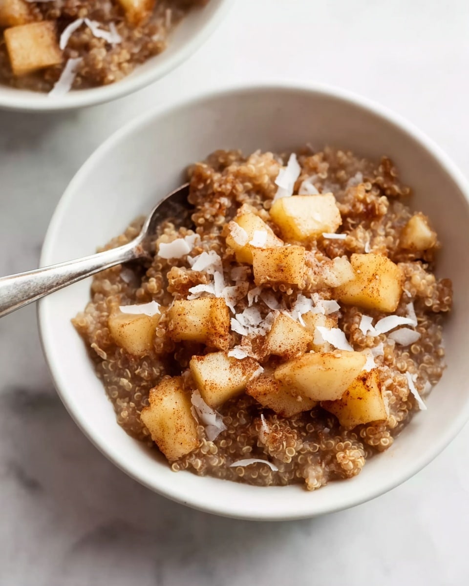 A white bowl filled with a warm mix of chopped cooked apples and brown quinoa, forming a textured, chunky base with a mix of light brown and beige colors. On top, several larger apple pieces dusted with cinnamon add a golden color and speckled appearance. Thin flakes of white coconut are sprinkled across the surface, adding a light contrast. The bowl is placed on a piece of burlap fabric, set against a smooth white marbled background with a soft light that highlights the colors and textures. In the background, a second white bowl with the same dish and a light brown ceramic jug are slightly blurred. Photo taken with an iphone --ar 4:5 --v 7