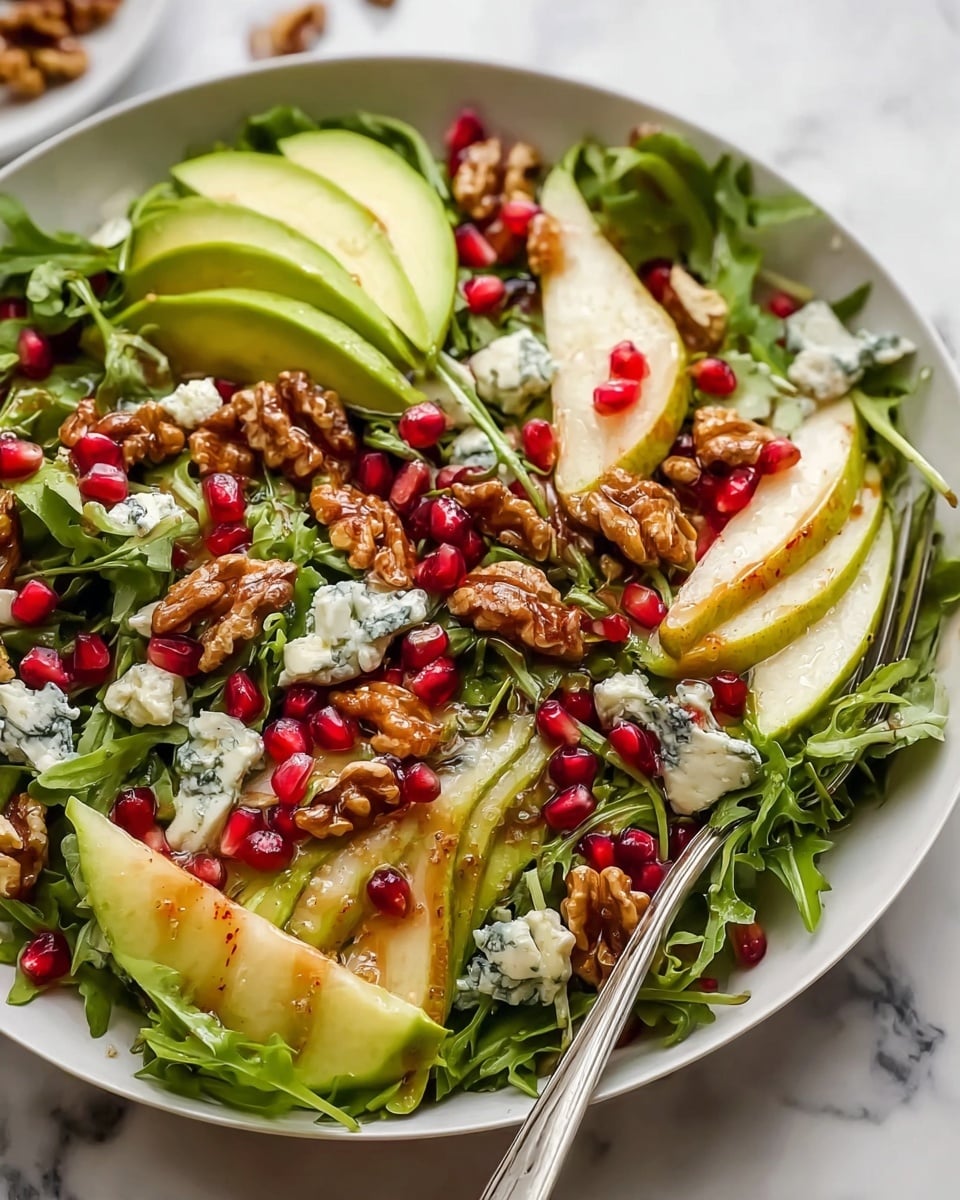 The image shows a fresh salad in a white bowl placed on a white marbled surface. The salad has a base layer of mixed green leafy vegetables including arugula and lettuce, creating a rich green bed. On top, there are scattered bright red pomegranate seeds and creamy chunks of blue cheese adding white and blue tones. Thin slices of light yellow-green apple are layered throughout, along with whole glossy brown walnuts that add texture and depth. A shiny dressing glistens over the ingredients, enhancing their colors. A silver fork is partially visible at the edge of the bowl. In the background, there is a hint of another bowl with greens and a decorative golden round object. photo taken with an iphone --ar 4:5 --v 7