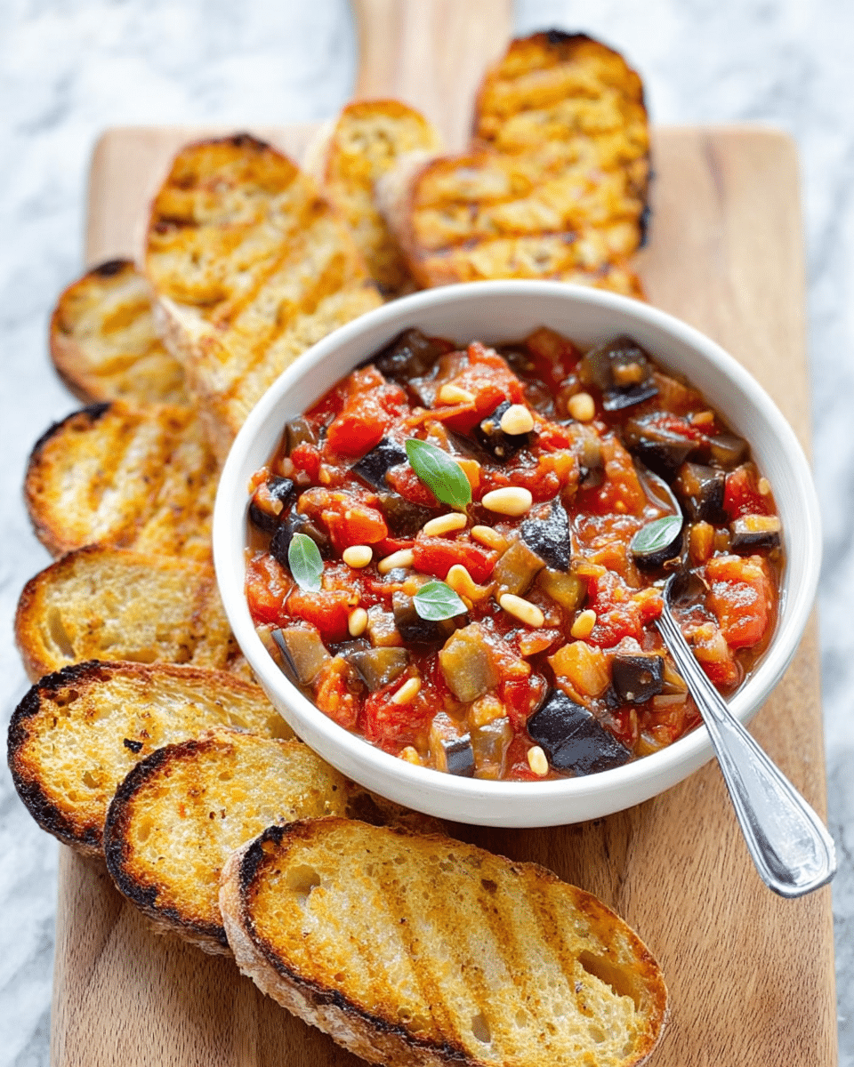 The image shows a white bowl filled with chunky vegetable stew, containing red tomato pieces, black olives, eggplant chunks, and pine nuts, topped with small green basil leaves. A silver spoon rests inside the bowl on the right side. Surrounding the bowl are several slices of toasted bread with a golden brown crust and grill marks, arranged neatly on a wooden board. The background surface is a white marbled texture. The overall scene is bright and inviting, with the warm colors of the dish contrasting against the neutral setting. photo taken with an iphone --ar 4:5 --v 7