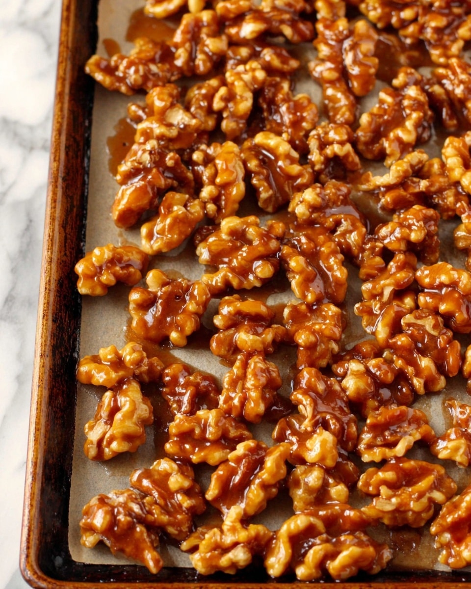 The image shows a close-up view of glossy caramelized walnuts spread across a baking tray lined with parchment paper. The individual walnut pieces are coated evenly in a thick, shiny caramel layer, giving them a rich amber color and a sticky texture. The walnuts are arranged in a single, uneven layer covering the tray completely with different cluster sizes visible. The baking tray edges are slightly worn and dark-colored, all placed on a white marbled surface. photo taken with an iphone --ar 4:5 --v 7
