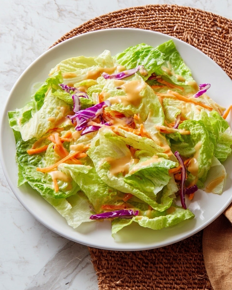 A white plate is filled with a simple salad made of torn light green iceberg lettuce leaves as the base, mixed with thin strips of purple cabbage and small pieces of orange shredded carrot scattered throughout. A light, creamy orange-colored dressing is drizzled unevenly on top of the layers. The plate rests on a white marbled textured surface, and to the side, there is a brown woven placemat. photo taken with an iphone --ar 4:5 --v 7