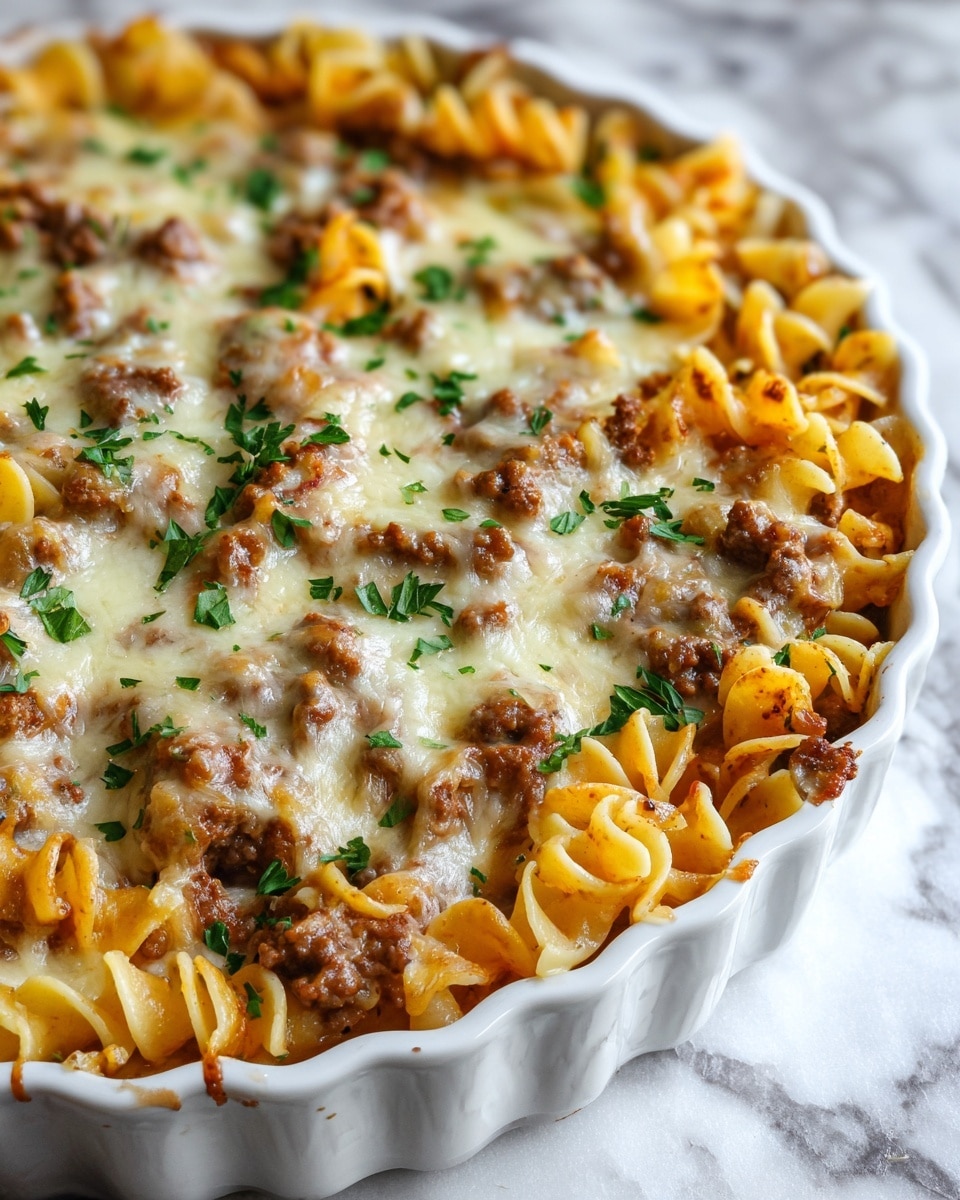 A close-up of a white round dish filled with baked pasta, showing two main layers: the bottom layer is light yellow wavy pasta noodles folded and mixed, and the top layer is cooked ground beef mixed with melted white and light golden cheese, with small green parsley leaves scattered on top. The edges of the pasta are slightly browned from baking, and the dish sits on a white marbled surface. photo taken with an iphone --ar 4:5 --v 7