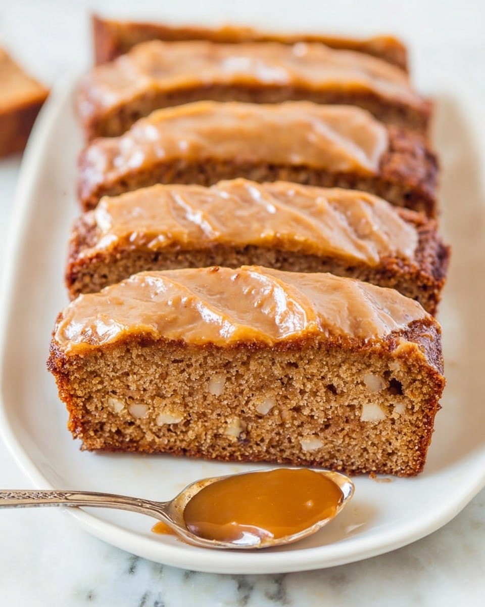 The image shows a white plate with five thick slices of a brown cake lined up closely. Each slice has one layer of moist cake with small nut pieces inside, topped with a smooth, light brown frosting that looks slightly shiny and spread unevenly. In front of the plate, there is a shiny silver spoon holding a dollop of caramel color sauce. The plate is placed on a white marbled surface. Photo taken with an iphone --ar 4:5 --v 7