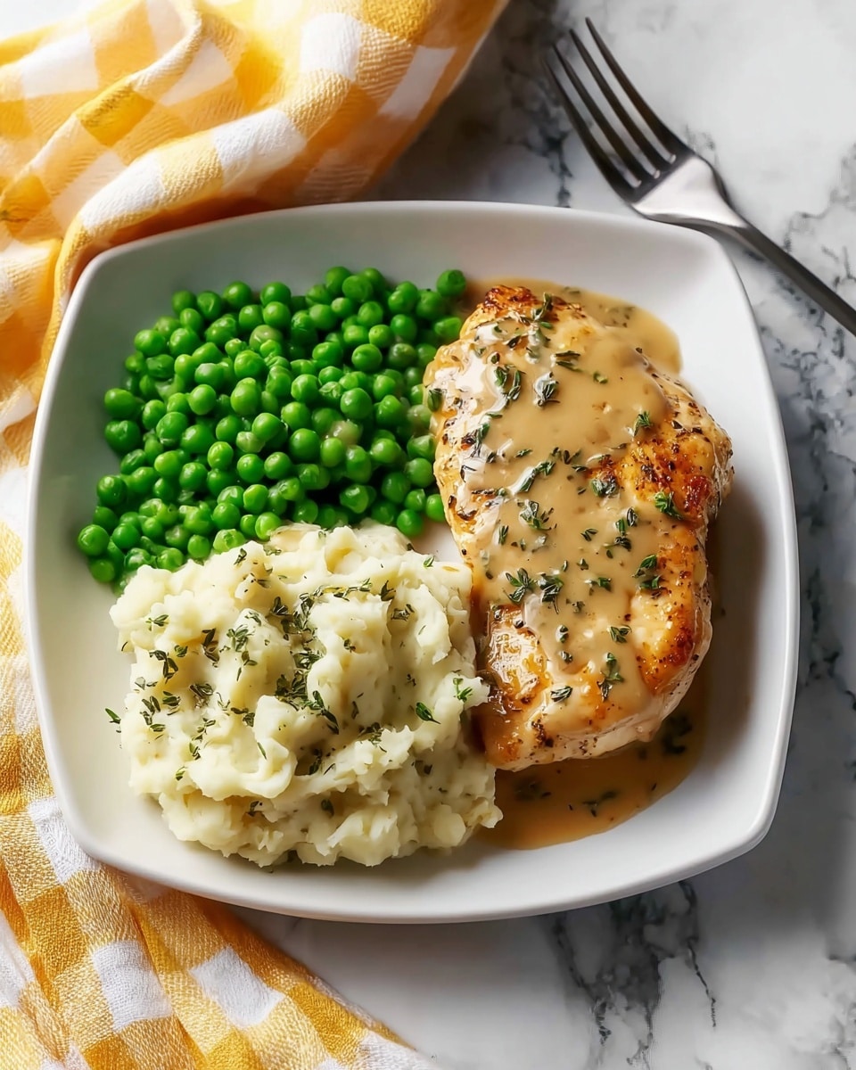 A square white plate on a white marbled surface holds a meal with three parts: first, bright green peas piled on the left side; second, creamy mashed potatoes with a smooth, fluffy texture topped with light brown gravy and green herb sprinkles on the top right; third, a single golden-brown grilled chicken breast covered with the same light brown herb gravy, positioned at the bottom center of the plate. A yellow and white checkered cloth is visible in the back left corner with a metal fork in the top right background. photo taken with an iphone --ar 4:5 --v 7